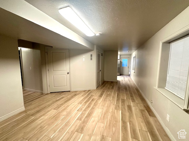Basement with baseboards, a textured ceiling, and light wood-type flooring