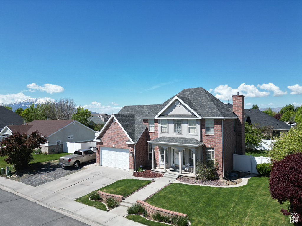 Traditional-style house featuring a chimney, driveway, brick siding, fence, and covered porch