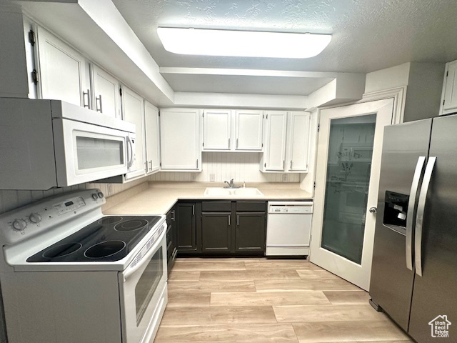 Kitchen featuring light countertops, a sink, white appliances, light wood-style flooring, and white cabinetry