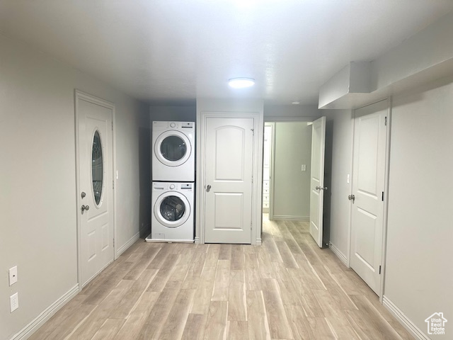Laundry area featuring baseboards, light wood finished floors, stacked washer and dryer, and laundry area