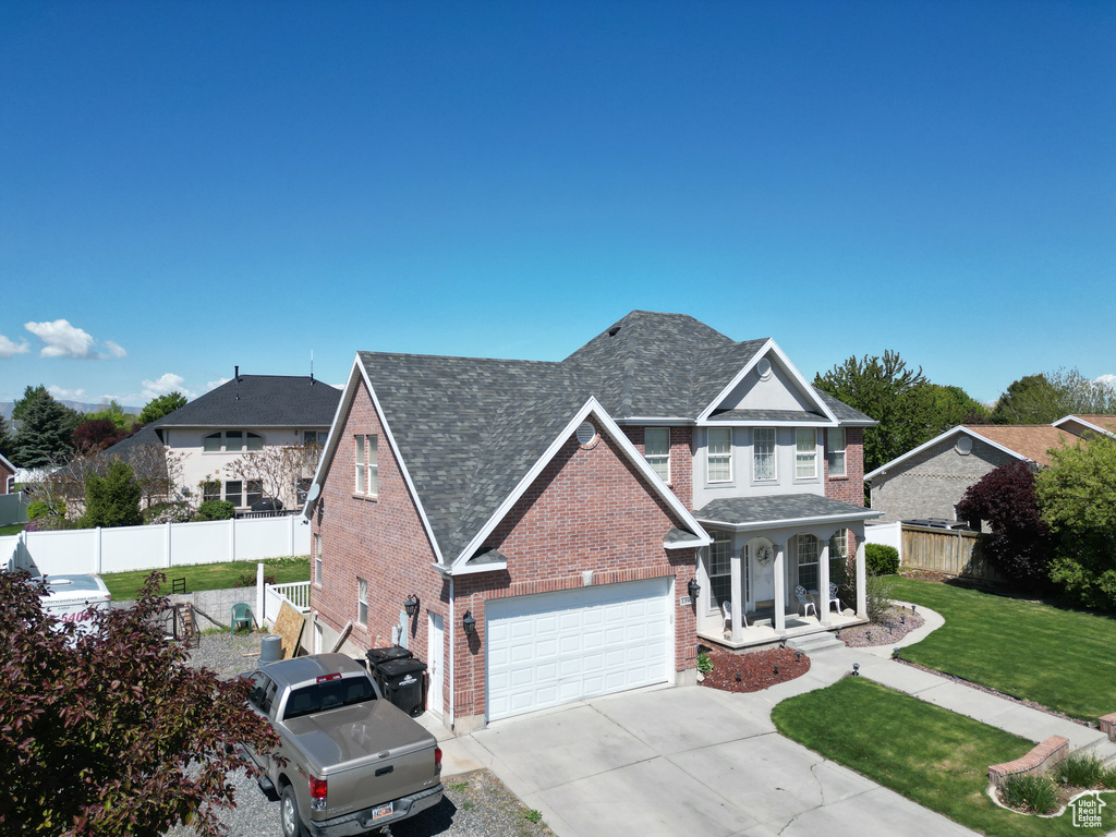Traditional-style home featuring covered porch, fence, brick siding, and a front yard