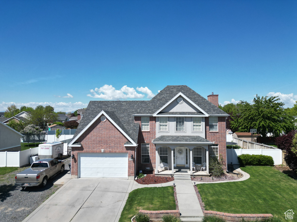 Traditional-style house featuring covered porch, concrete driveway, brick siding, and fence