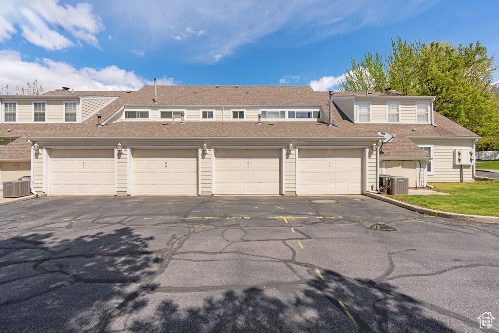 Townhome / multi-family property with central air condition unit, roof with shingles, and community garages