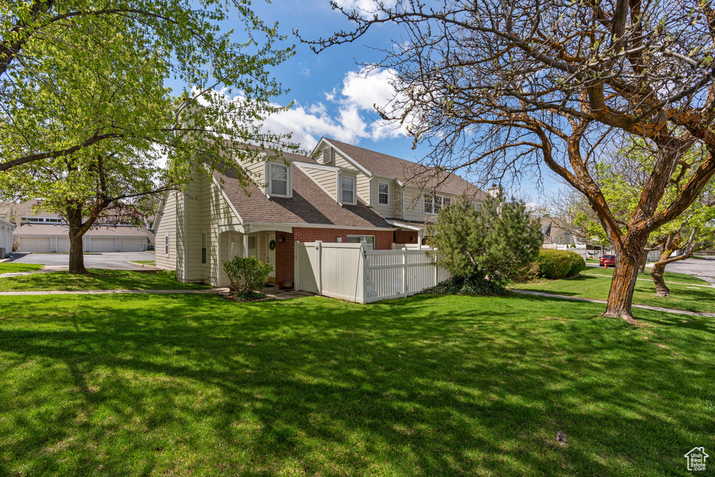 View of property exterior with a lawn, fence, a shingled roof, and brick siding