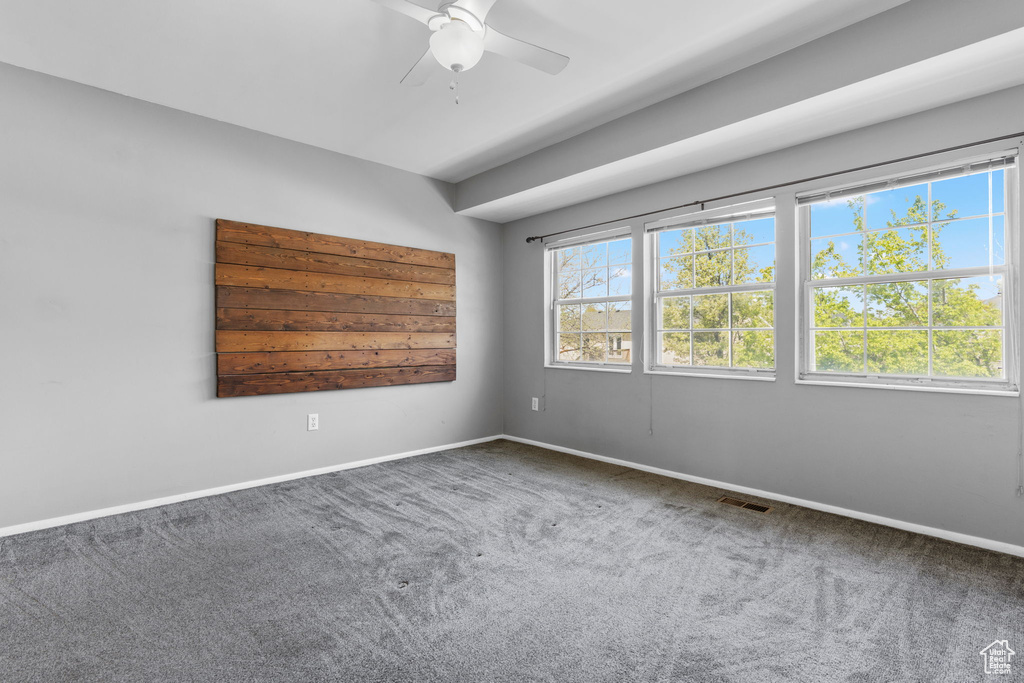 Carpeted empty room with baseboards, a ceiling fan, and visible vents
