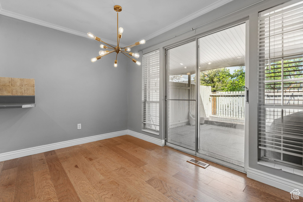 Unfurnished dining area with wood finished floors, a chandelier, baseboards, ornamental molding, and visible vents