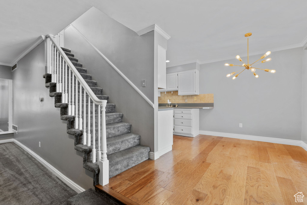 Stairway featuring visible vents, baseboards, an inviting chandelier, wood finished floors, and crown molding