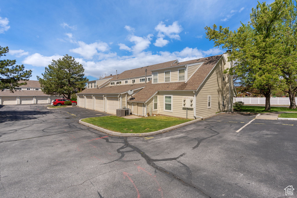 Exterior space with central air condition unit, roof with shingles, community garages, and fence