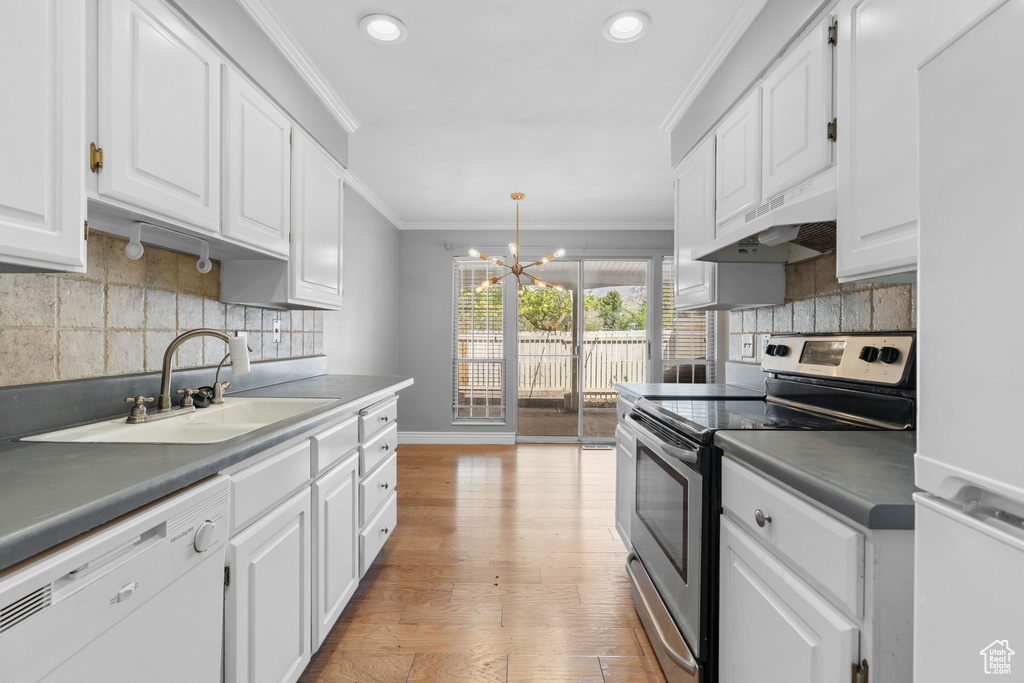 Kitchen featuring a sink, a chandelier, white appliances, under cabinet range hood, and ornamental molding