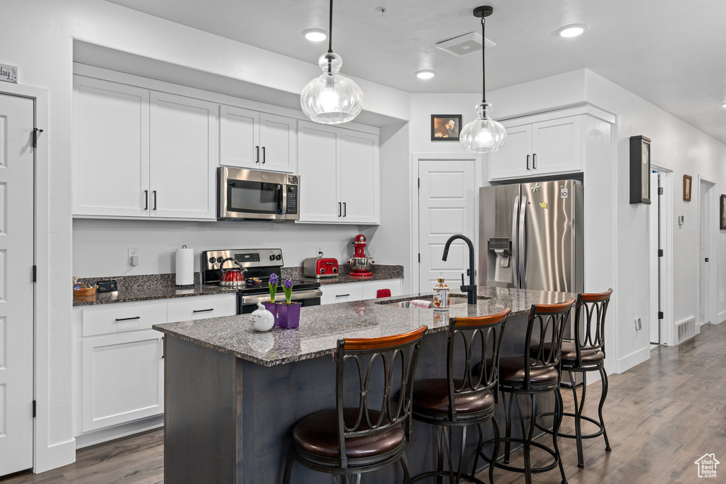 Kitchen with stainless steel appliances, a breakfast bar, wood finished floors, visible vents, and a sink