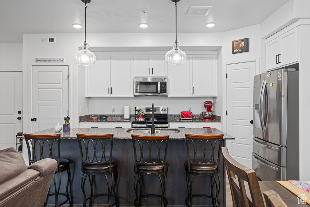 Kitchen featuring white cabinets, appliances with stainless steel finishes, light stone counters, and visible vents