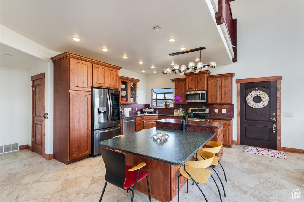 Kitchen with dark countertops, tasteful backsplash, an island with sink, appliances with stainless steel finishes, and visible vents