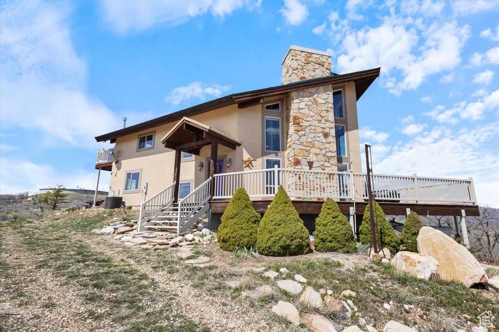 View of front of home featuring central air condition unit, a chimney, stucco siding, and a deck