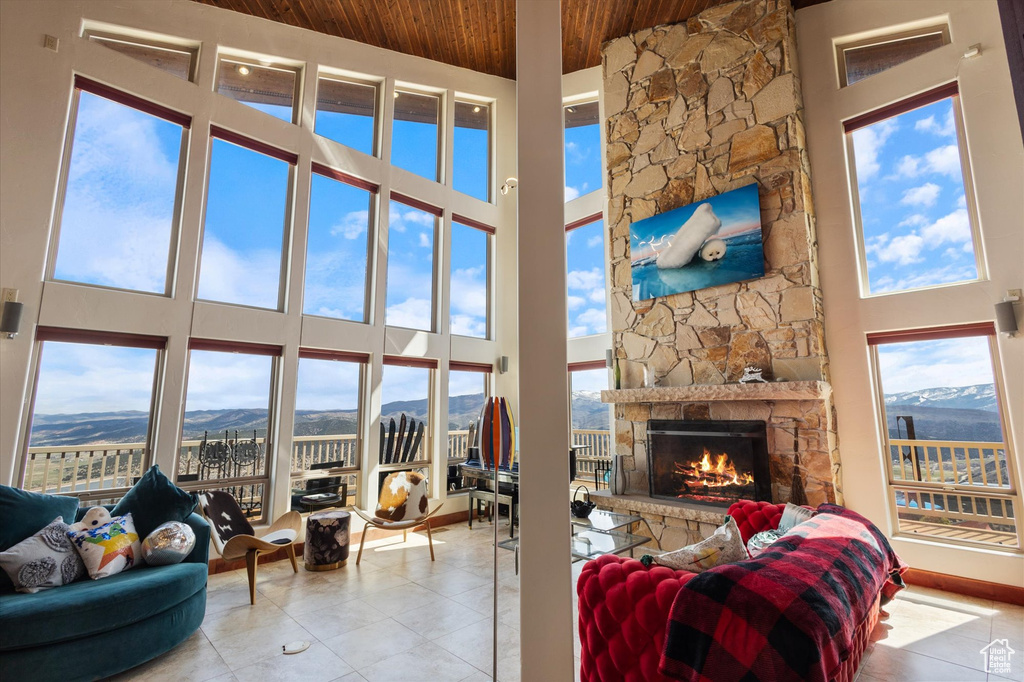 Tiled living area with a stone fireplace, a high ceiling, wood ceiling, and a mountain view