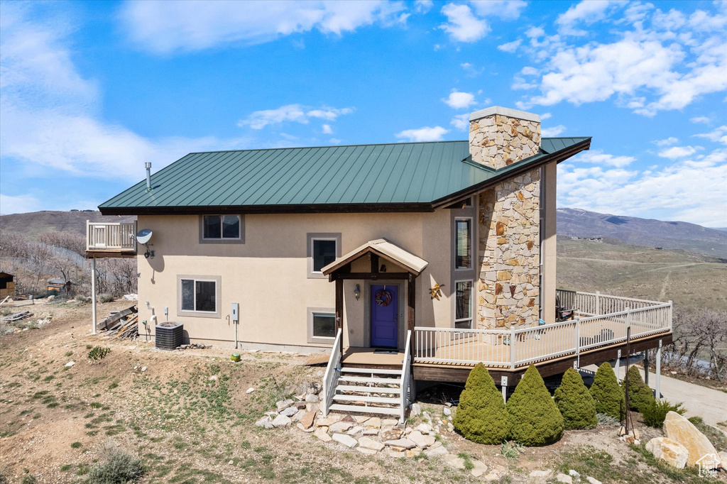 Rear view of property featuring a deck with mountain view, stone siding, metal roof, stucco siding, and a standing seam roof