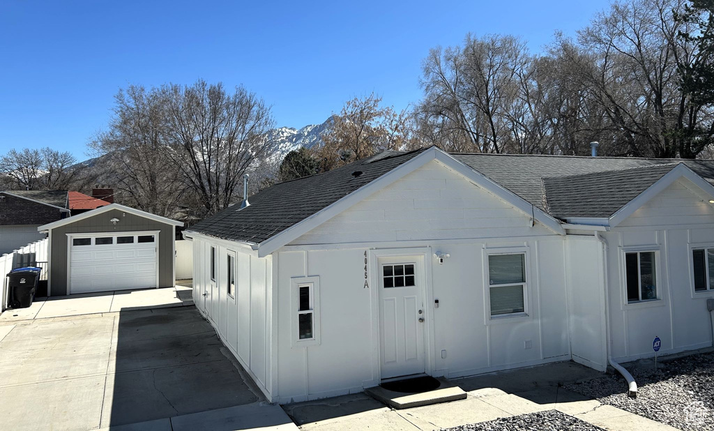 Single story home featuring a shingled roof, board and batten siding, concrete driveway, an outbuilding, and a mountain view