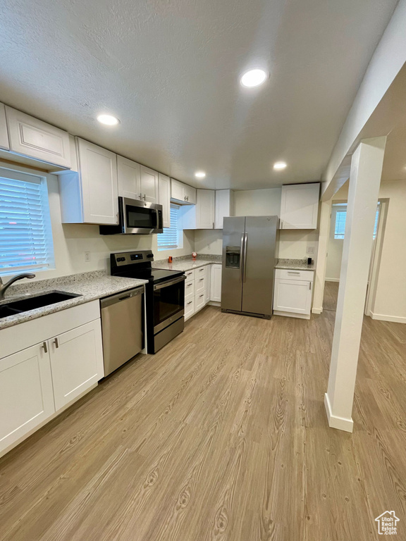 Kitchen featuring stainless steel appliances, light wood finished floors, white cabinetry, a sink, and recessed lighting