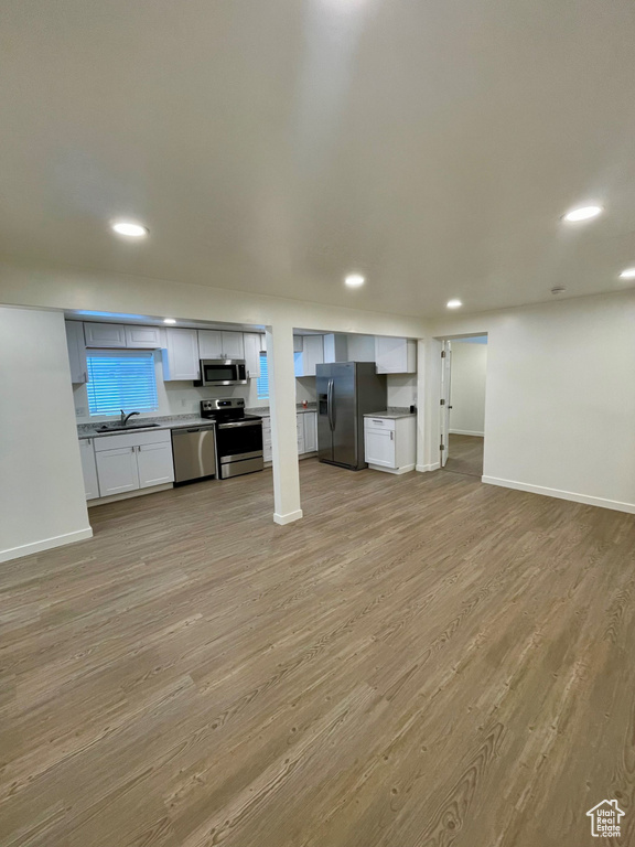Below grade area with fridge with ice dispenser, a sink, light wood-style flooring, baseboards, and recessed lighting