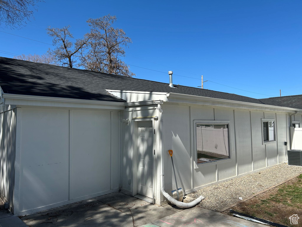 Back of property with roof with shingles, central AC unit, and board and batten siding