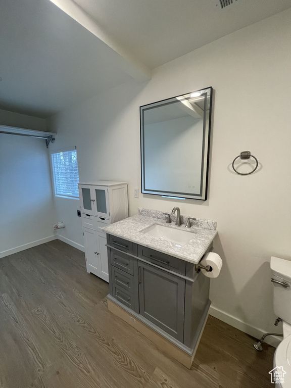 Half bathroom with toilet, wood finished floors, baseboards, and vanity