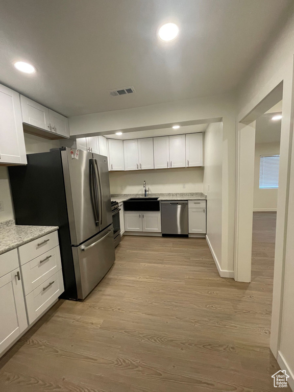 Kitchen with stainless steel appliances, a sink, wood finished floors, white cabinets, and recessed lighting