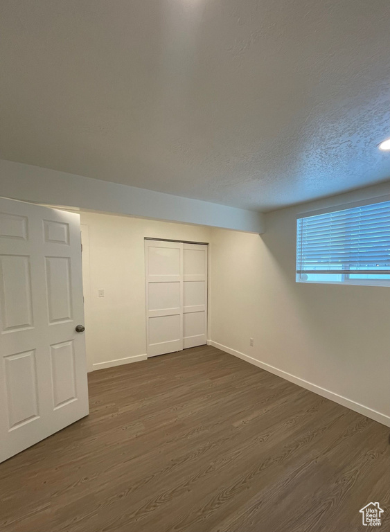 Unfurnished bedroom featuring dark wood-type flooring, baseboards, a closet, and a textured ceiling