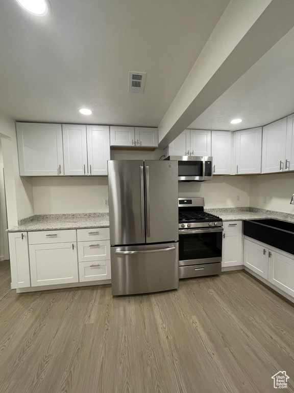 Kitchen with stainless steel appliances, a sink, white cabinets, light wood-type flooring, and recessed lighting