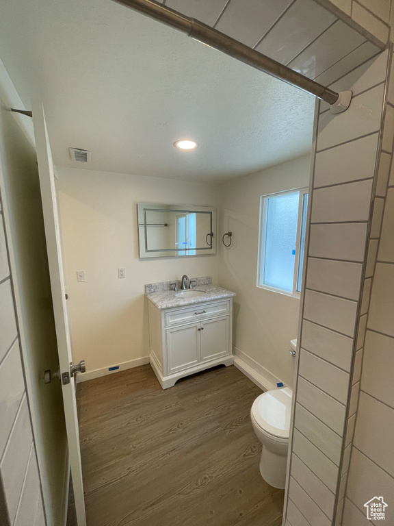 Bathroom featuring wood finished floors, baseboards, toilet, vanity, and recessed lighting