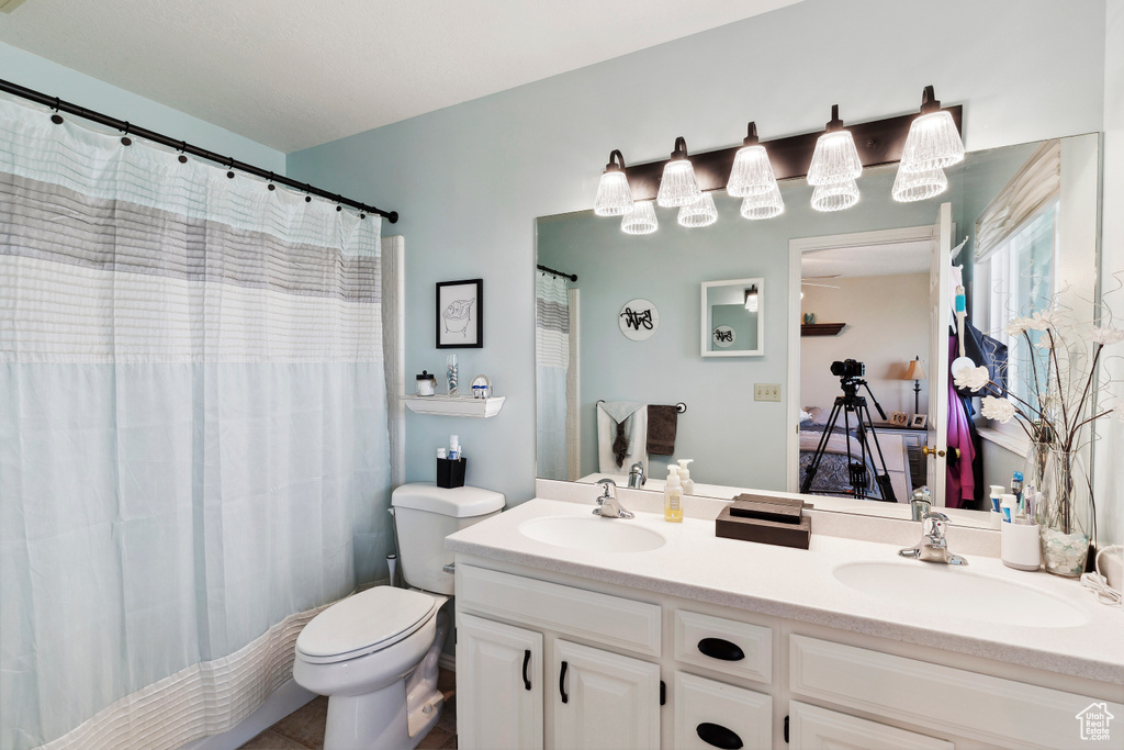 Bathroom featuring double vanity, a sink, curtained shower, and toilet