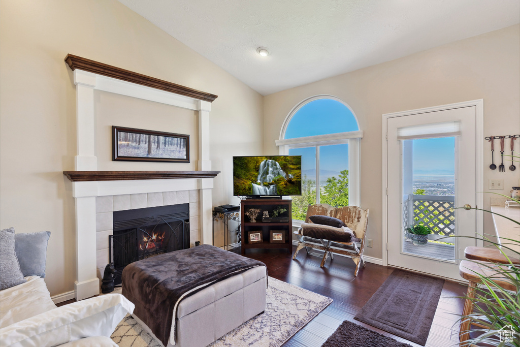 Living room featuring dark wood-style floors, vaulted ceiling, and a tile fireplace