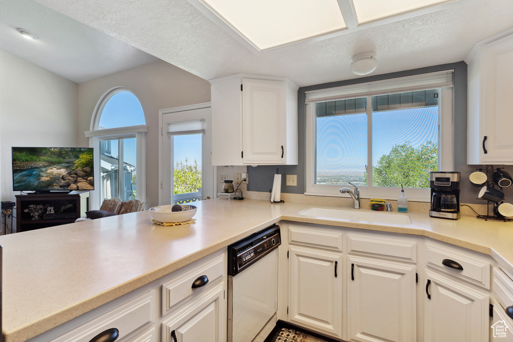 Kitchen with dishwasher, a sink, light countertops, a peninsula, and white cabinetry