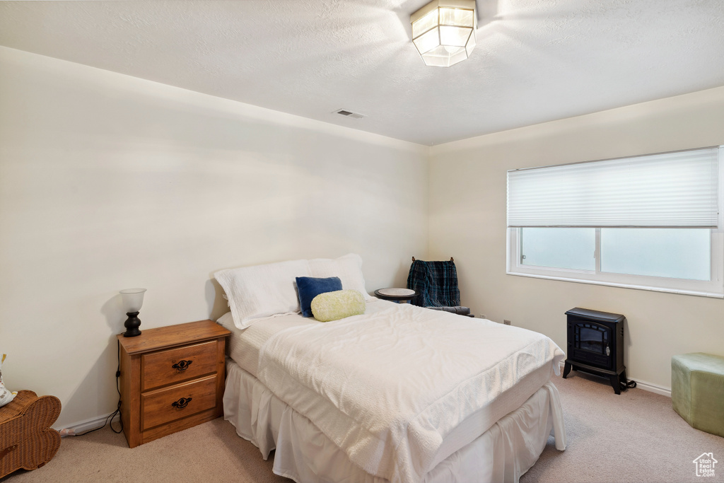 Bedroom with light colored carpet, a wood stove, baseboards, and visible vents