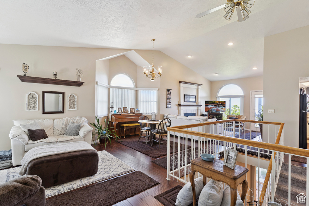 Living area with lofted ceiling, dark wood-style floors, recessed lighting, a tiled fireplace, and ceiling fan with notable chandelier