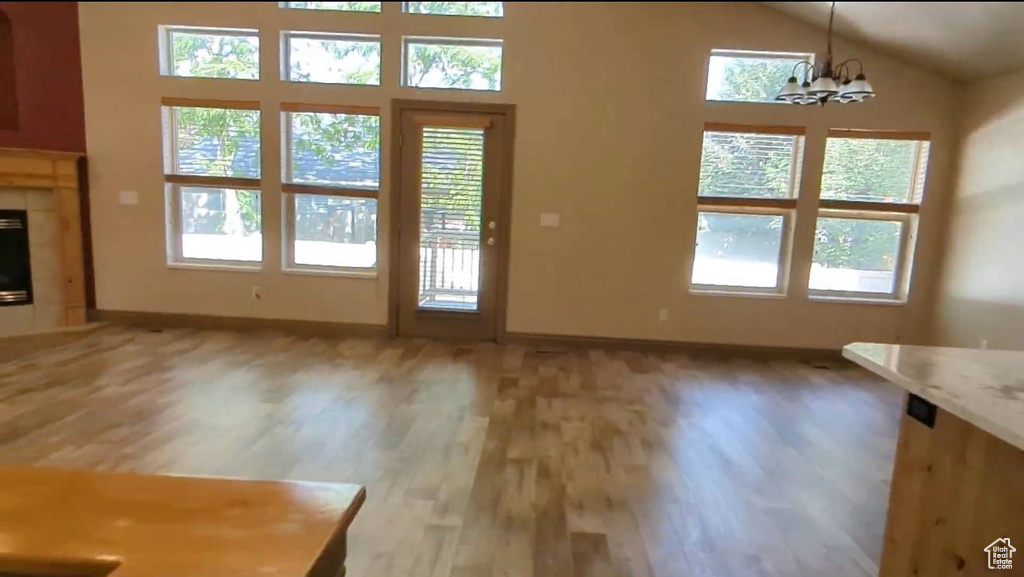 Unfurnished living room featuring light wood-type flooring, healthy amount of natural light, baseboards, and lofted ceiling
