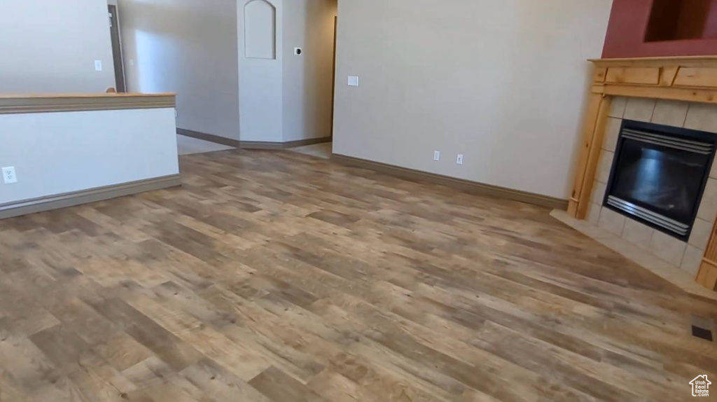 Unfurnished living room featuring wood finished floors, a tiled fireplace, and baseboards
