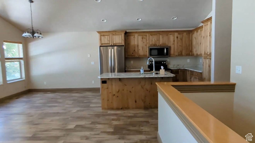 Kitchen featuring appliances with stainless steel finishes, a sink, light wood-style flooring, an island with sink, and a chandelier