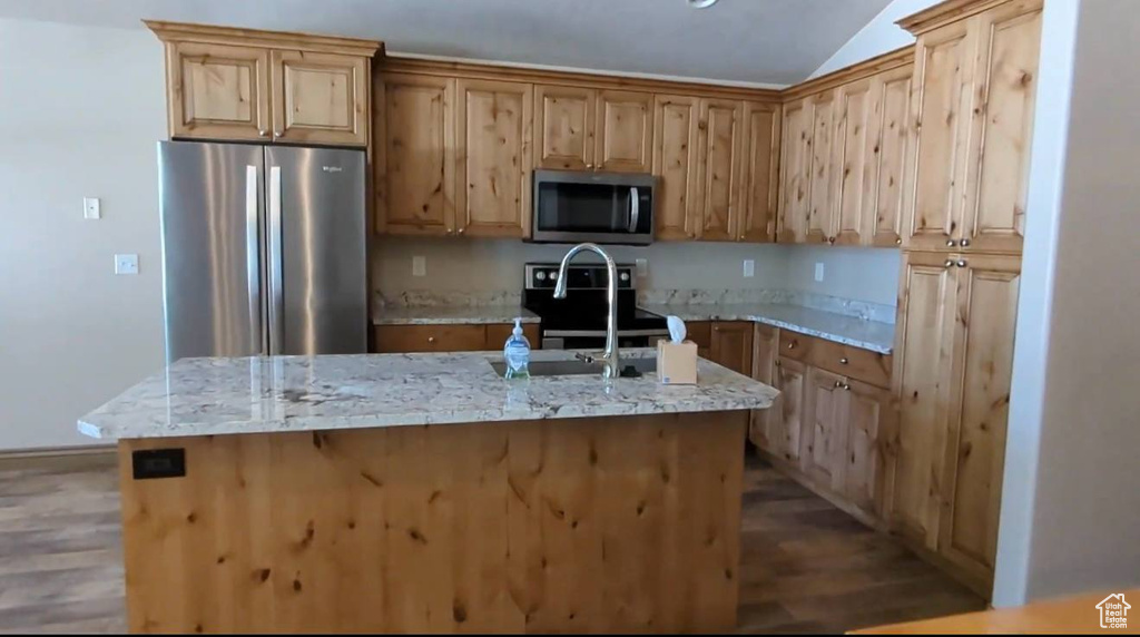 Kitchen with appliances with stainless steel finishes, wood finished floors, a sink, a center island with sink, and vaulted ceiling