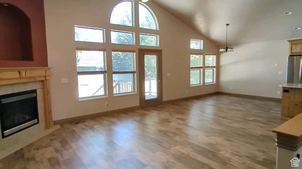 Unfurnished living room featuring healthy amount of natural light, light wood-type flooring, baseboards, and high vaulted ceiling