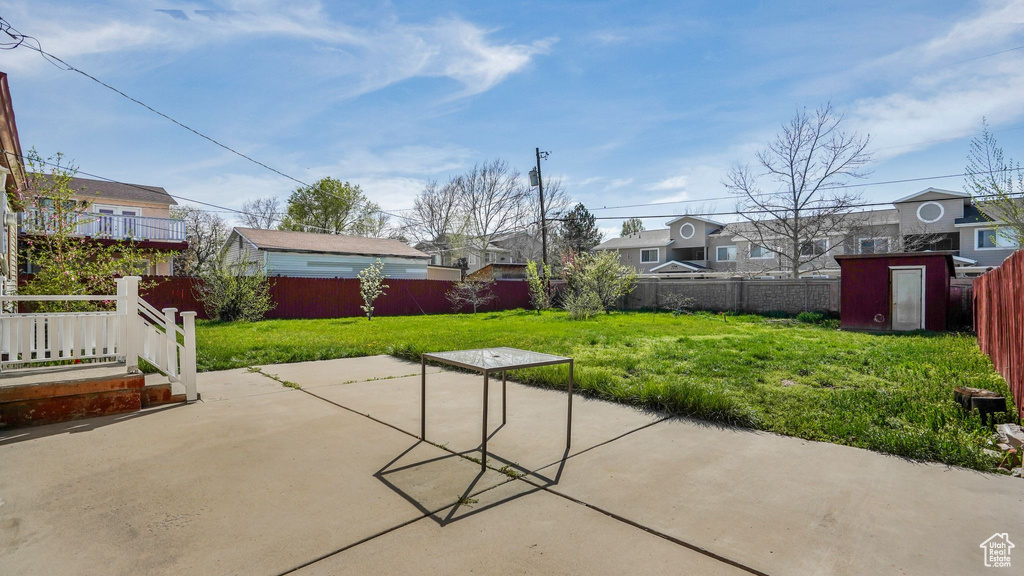 View of patio with a storage unit, an outbuilding, a fenced backyard, and a residential view