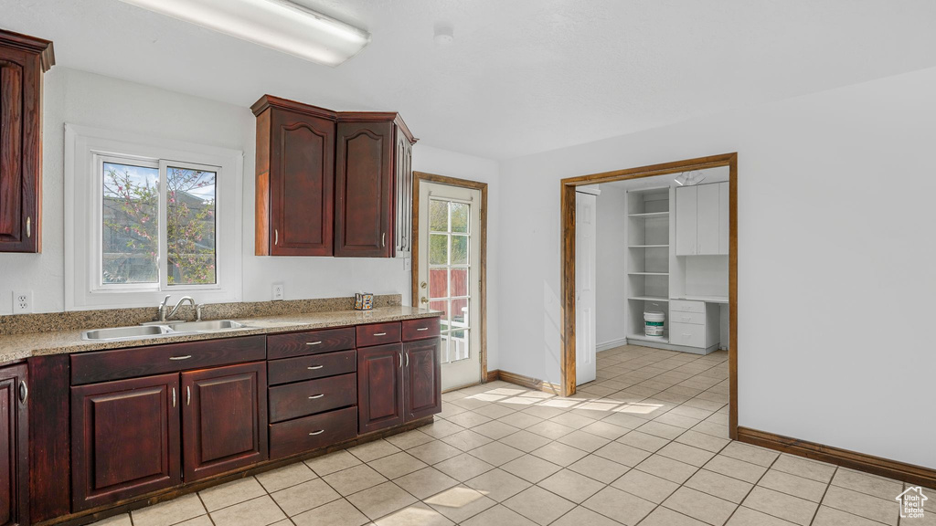 Kitchen featuring light tile patterned floors, baseboards, a sink, and plenty of natural light