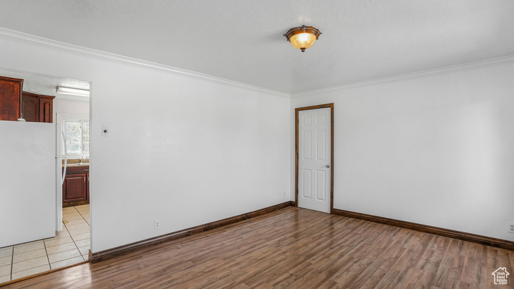 Empty room with baseboards, crown molding, and light wood-style floors