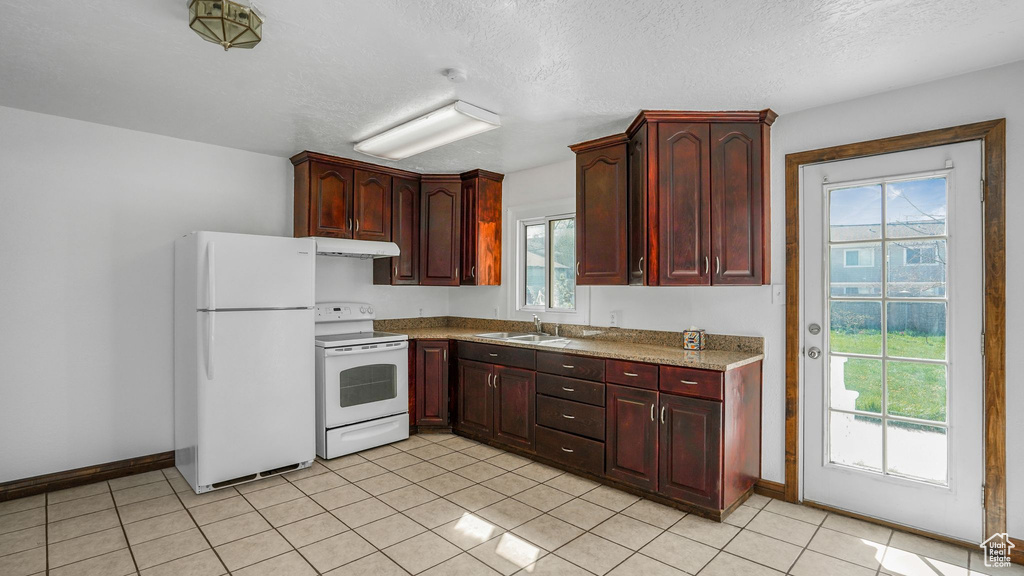 Kitchen with baseboards, under cabinet range hood, a sink, and white appliances