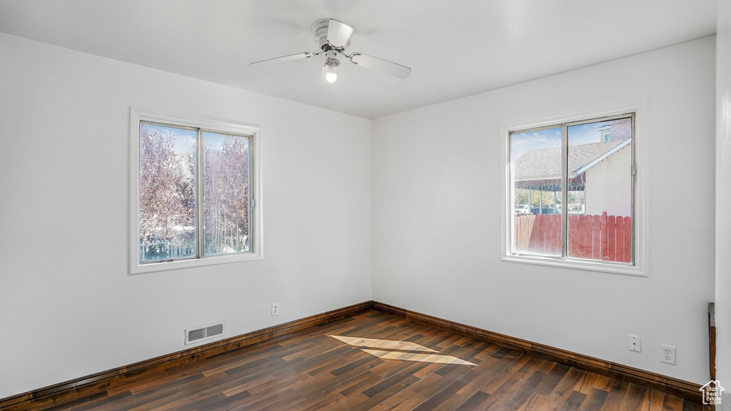 Empty room with dark wood finished floors, visible vents, baseboards, and a healthy amount of sunlight