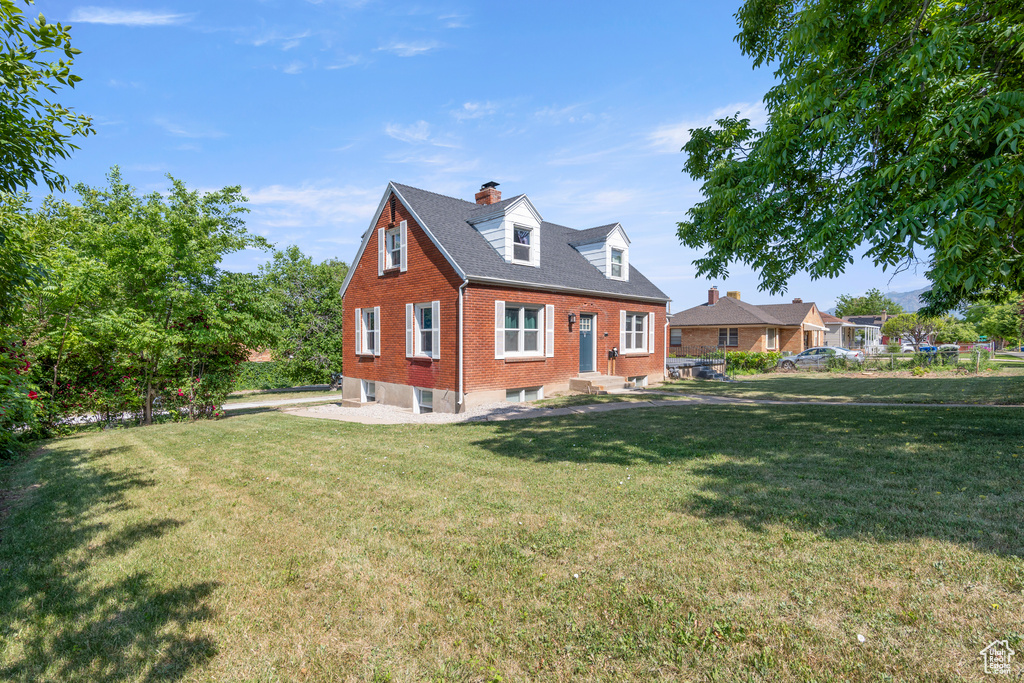 Cape cod house featuring brick siding, a chimney, a front yard, and entry steps