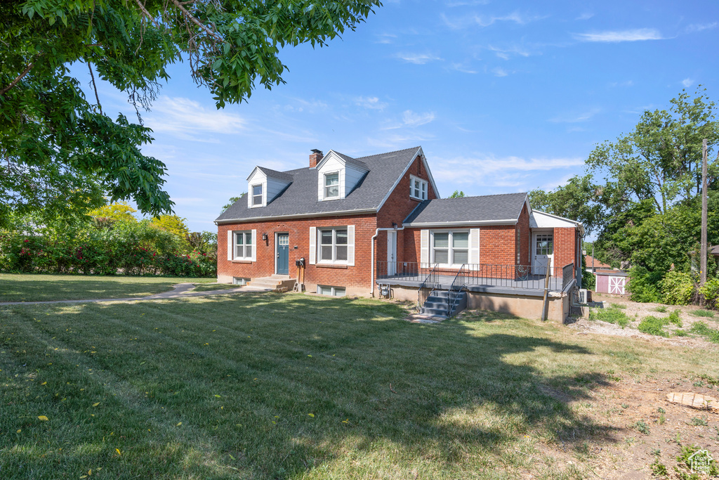 Cape cod home featuring brick siding, a chimney, and a front yard