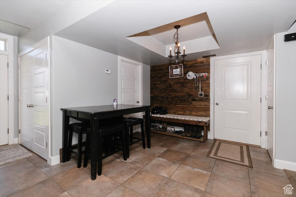 Dining room with a raised ceiling, baseboards, a chandelier, and wood walls