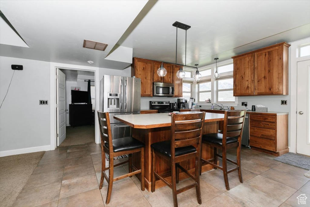 Kitchen with stainless steel appliances, brown cabinets, a center island, light countertops, and a breakfast bar area
