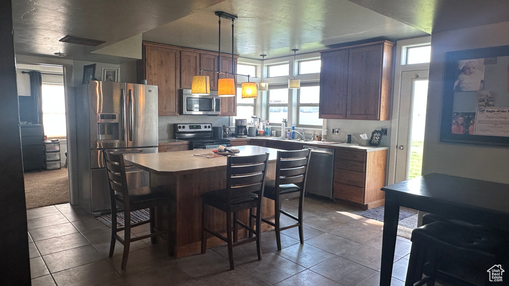 Kitchen with hanging light fixtures, dark tile patterned flooring, a breakfast bar area, stainless steel appliances, and a center island