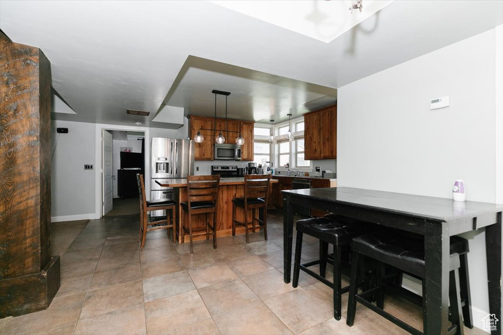 Kitchen featuring stainless steel appliances, hanging light fixtures, brown cabinets, a breakfast bar, and baseboards