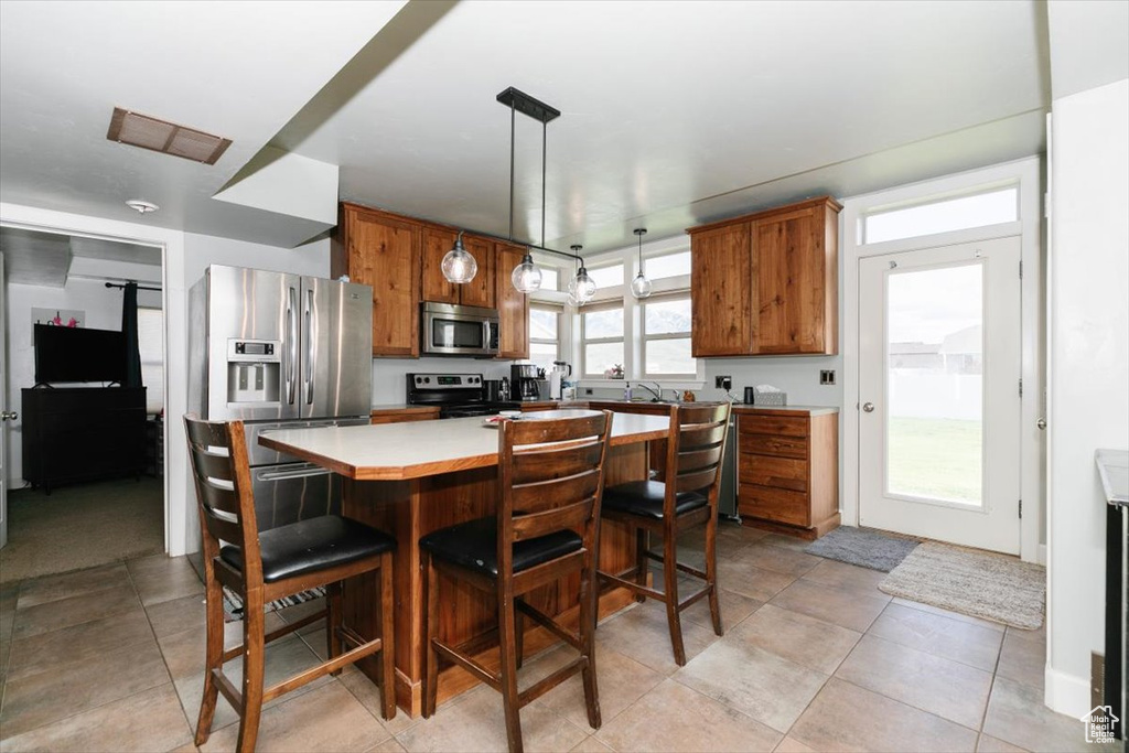 Kitchen with appliances with stainless steel finishes, brown cabinets, light countertops, a kitchen island, and a breakfast bar area